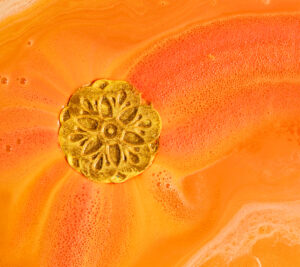 Rangoli Dreams Badebombe löst sich in einer Badewanne auf. Die goldene Blume verzaubert das Wasser in Orang- und Gelbtöne. 