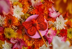 Ein oranges Damas del Sol Schaumbad liegt umringt von bunten Blumen auf einem rosa Podest