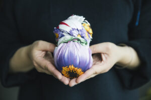 A close-up of a person's hands holding a Lush knot wrap which is tied around a bath bomb