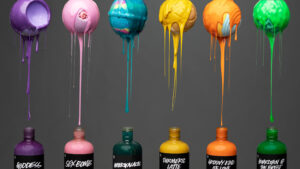 Lush Shower gels are lined up. Above them, bath bombs of corresponding colours, covered in the shower gel drip shower gel down into the bottles against a grey background