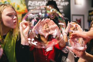 Several people on a Lush shop floor are blowing giant soapy bubbles through their hands