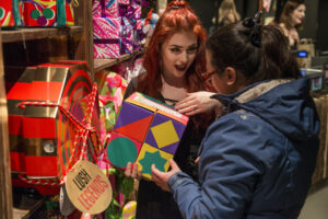 A Lush employee with bright red hair shows a Lush gift box to a customer on the shop floor
