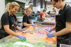 Lush manufacturing staff are standing on the factory floor pressing bath bombs which contain shades of green, peach and pink