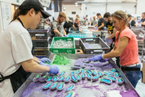 Lush compounders are working around a pressing table, making Aubergine bath bomb