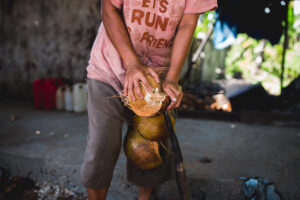 A person stands in the street compressing coconuts with their hands