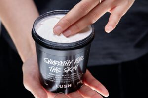 A person dips their fingers into a pot of Sympathy for the Skin body lotion