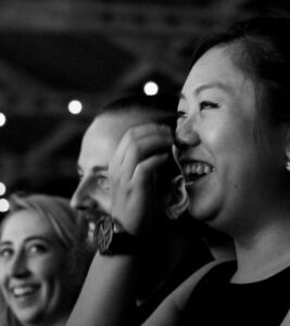 A black and white close-up image of 3 people sitting in an audience, smiling and laughing
