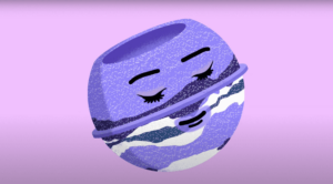 Thumbnail for the video '27 Years in Review' video. An animated purple Goddess bath bomb with it's eyes closed, smiling against a pink background,