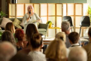 Founder Ro is stood talking at a Green Hub event - She has pink shoulder length hair and is wearing a light green flowy dress